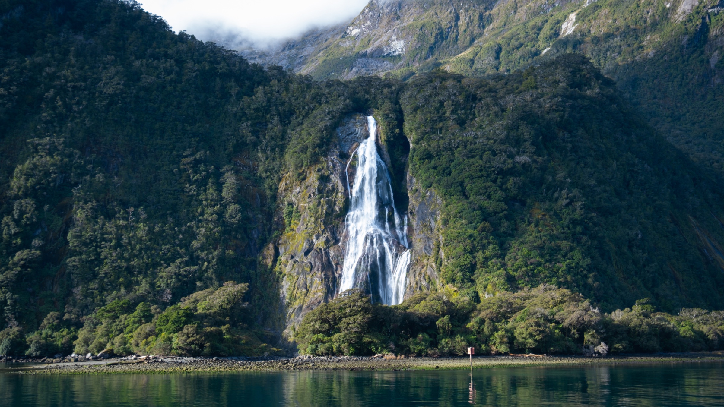Misty fjord with a waterfall dropping through dark green cliffs into still water